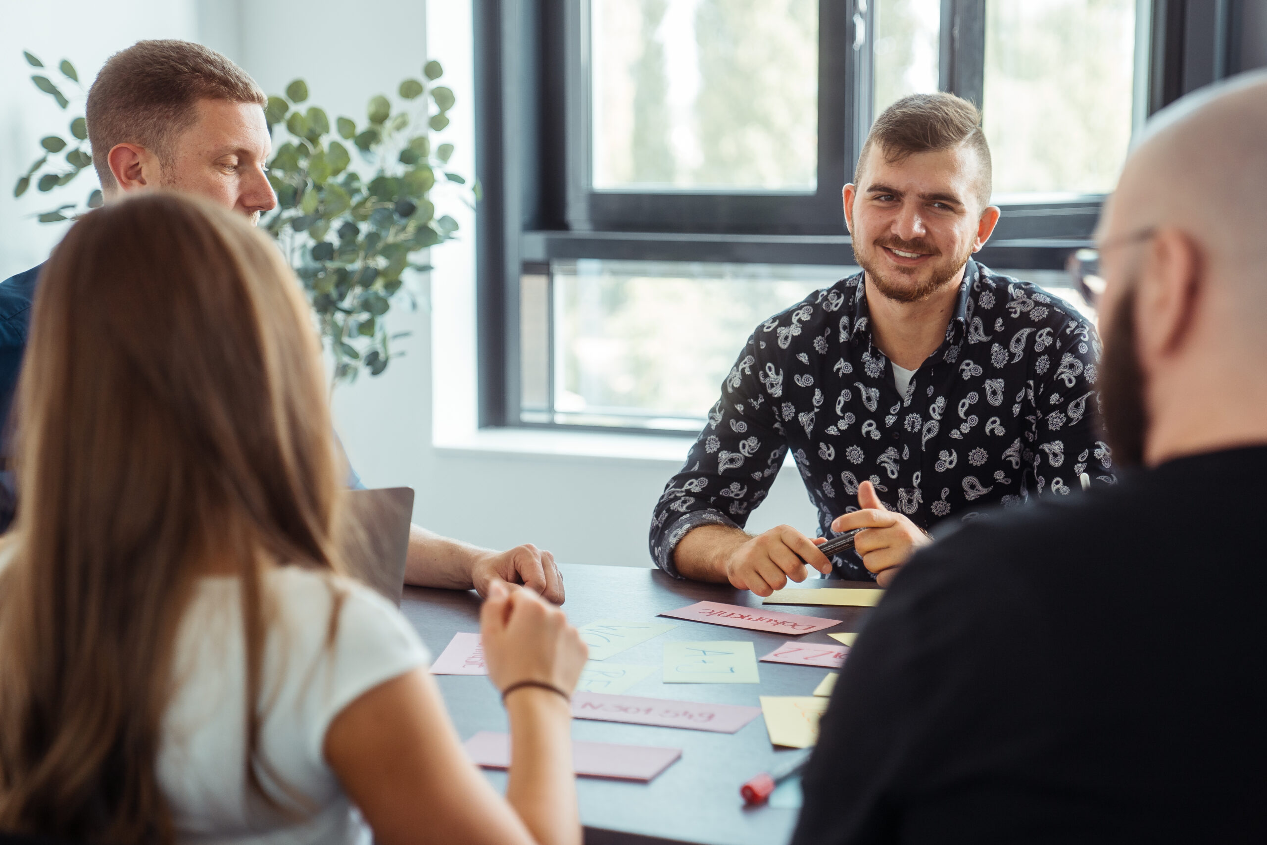 Momentaufnahme eines Workshops, bei dem die Teilnehmenden in einem Meetingraum an einem großen Tisch sitzen, auf dem sich beschriebene, bunte Karteikarten befinden.