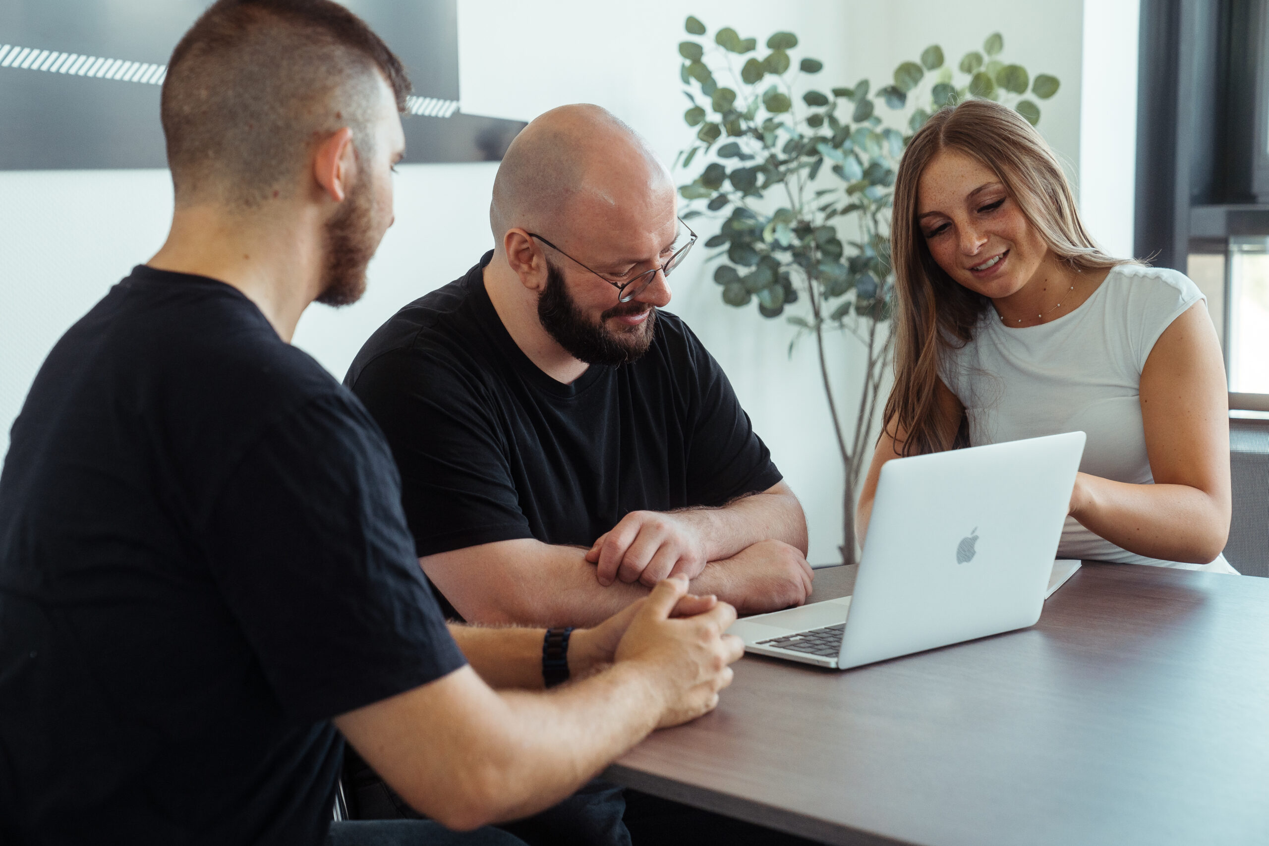Drei Personen sitzen an einem Meetingtisch. Vor ihnen steht ein Laptop.